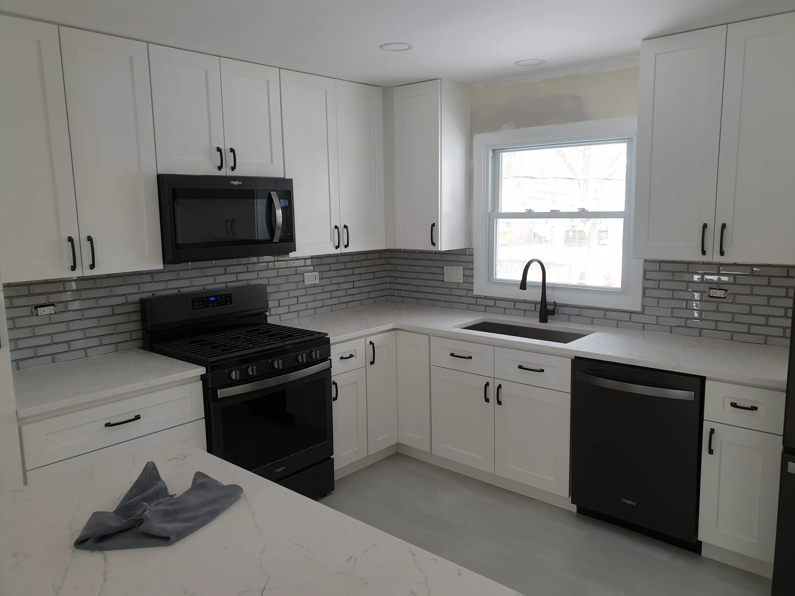 Modern kitchen renovation featuring white cabinets, grey backsplash, and stainless steel appliances
