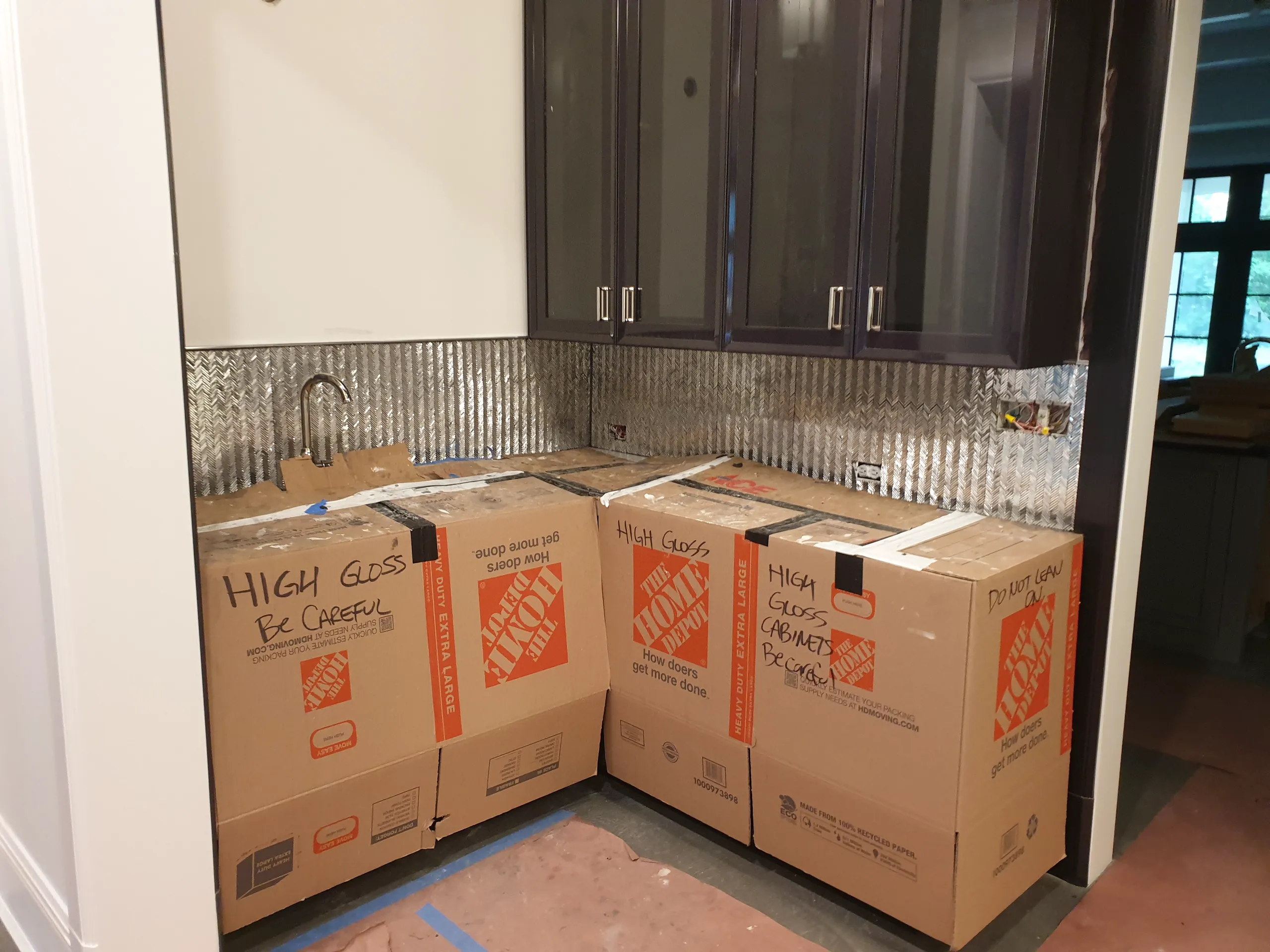 Kitchen renovation in progress with cabinets packed in boxes and a metallic backsplash visible