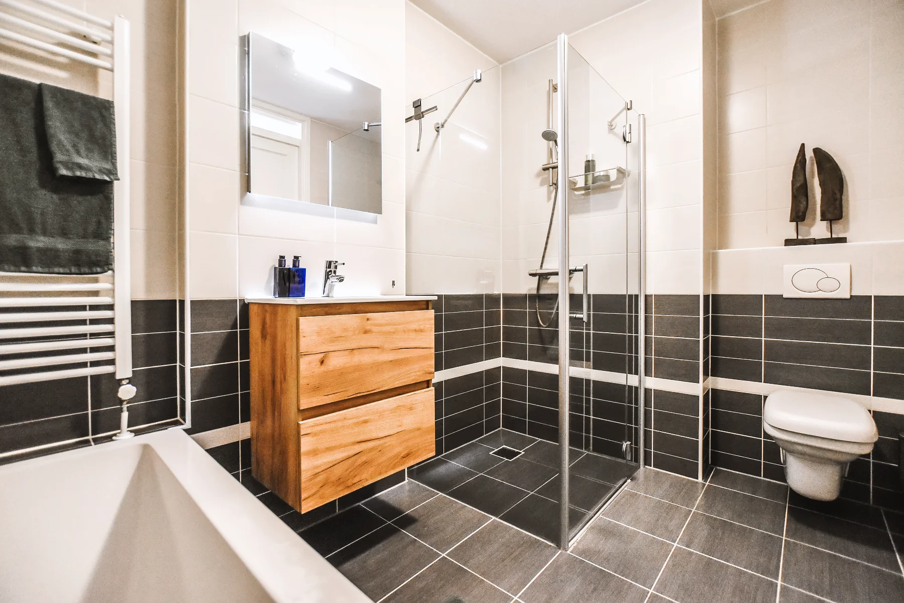 Modern bathroom with glass shower, wooden vanity, and grey tiles, showcasing a shower remodel