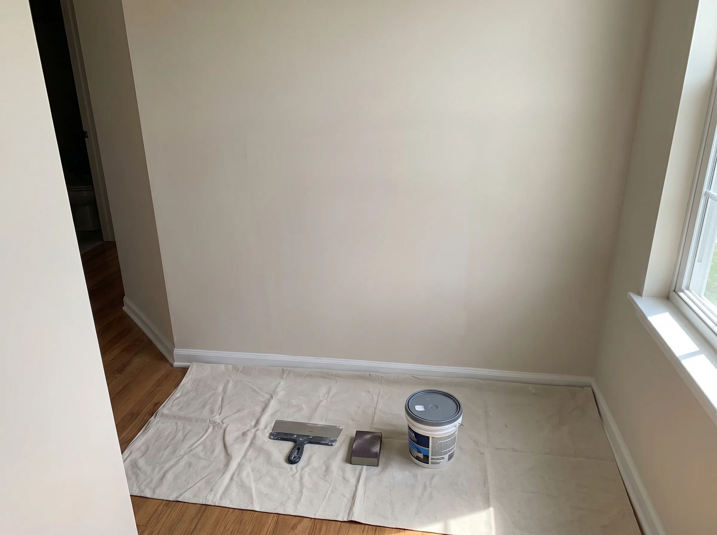 Interior painting supplies arranged on a drop cloth in a room corner