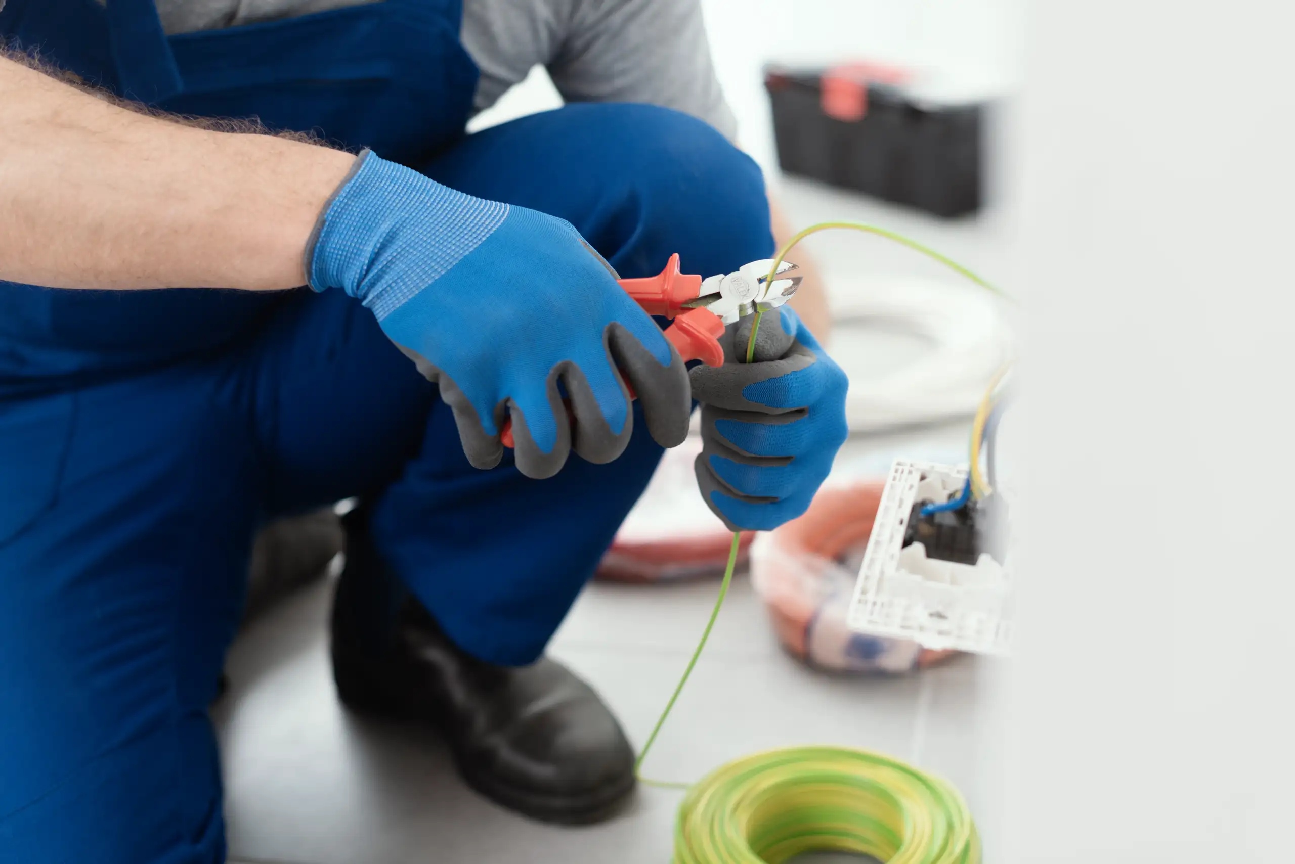 A technician in blue gloves uses wire cutters while performing electrical services