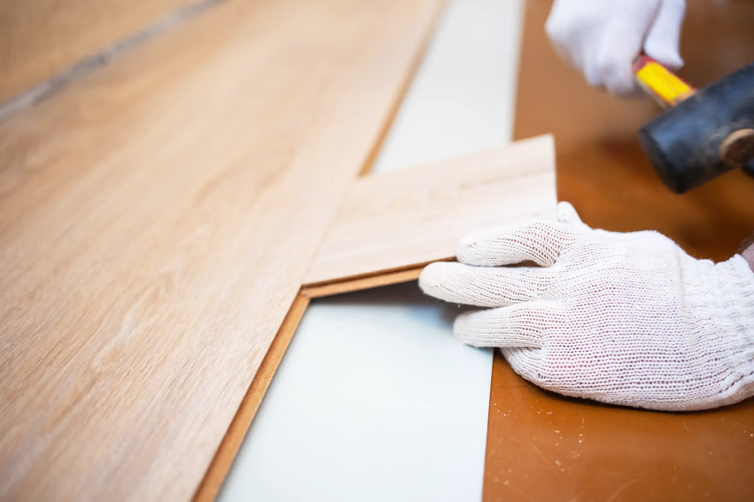 A person installing laminate flooring with a hammer and hands covered in gloves