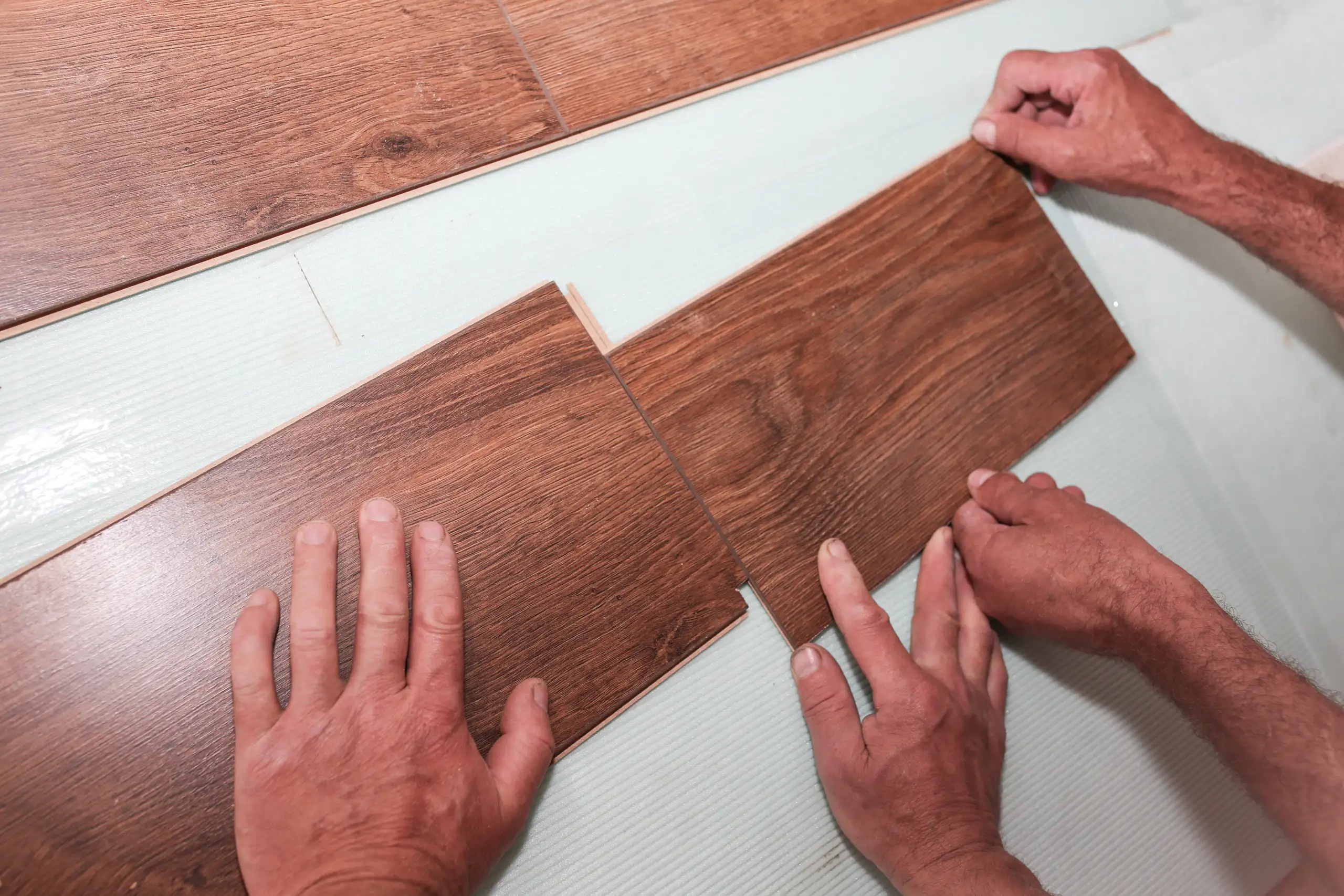 Installing laminate flooring with hands carefully fitting together planks
