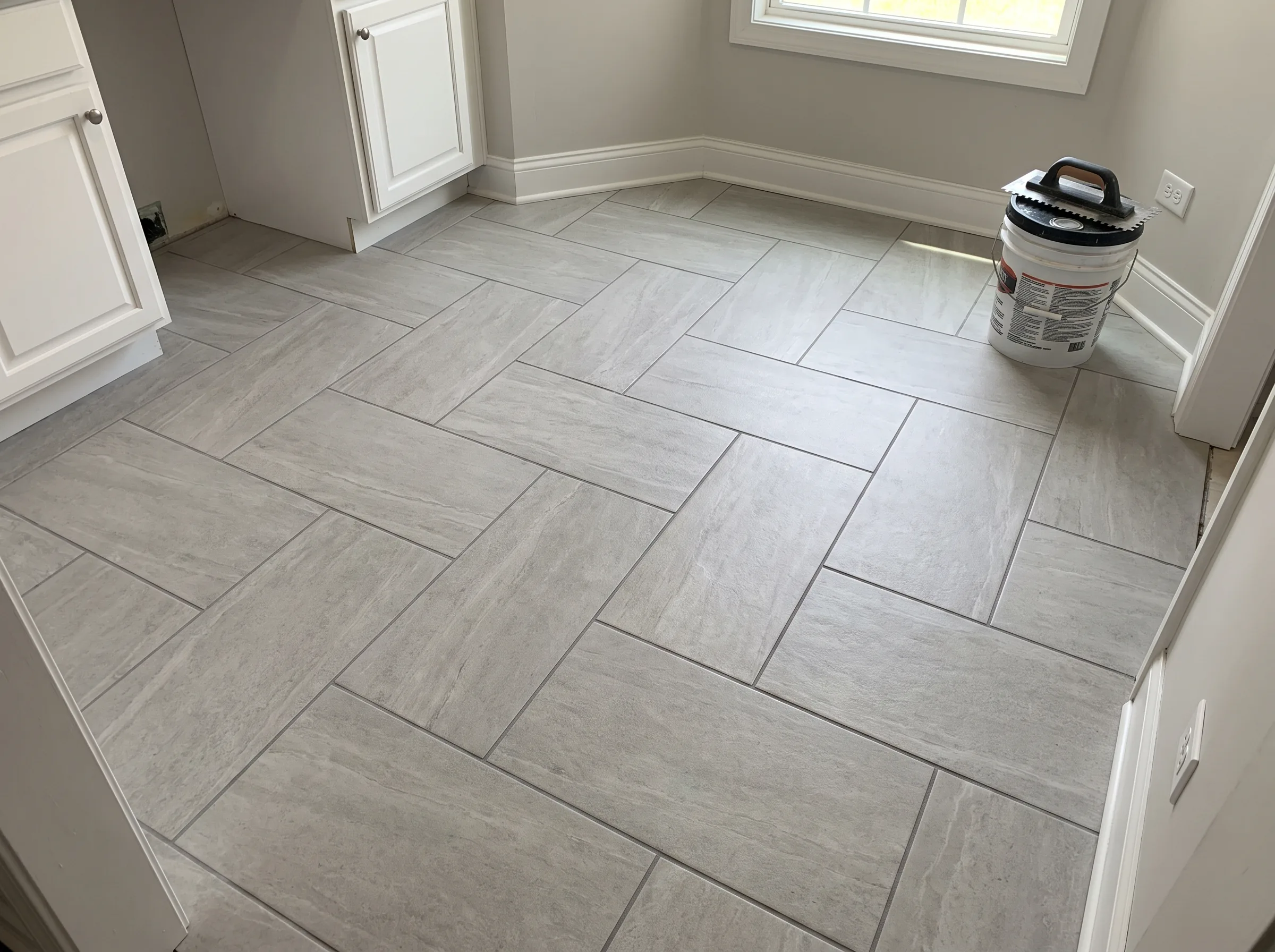 Newly installed grey ceramic tile flooring in a kitchen area with white cabinetry