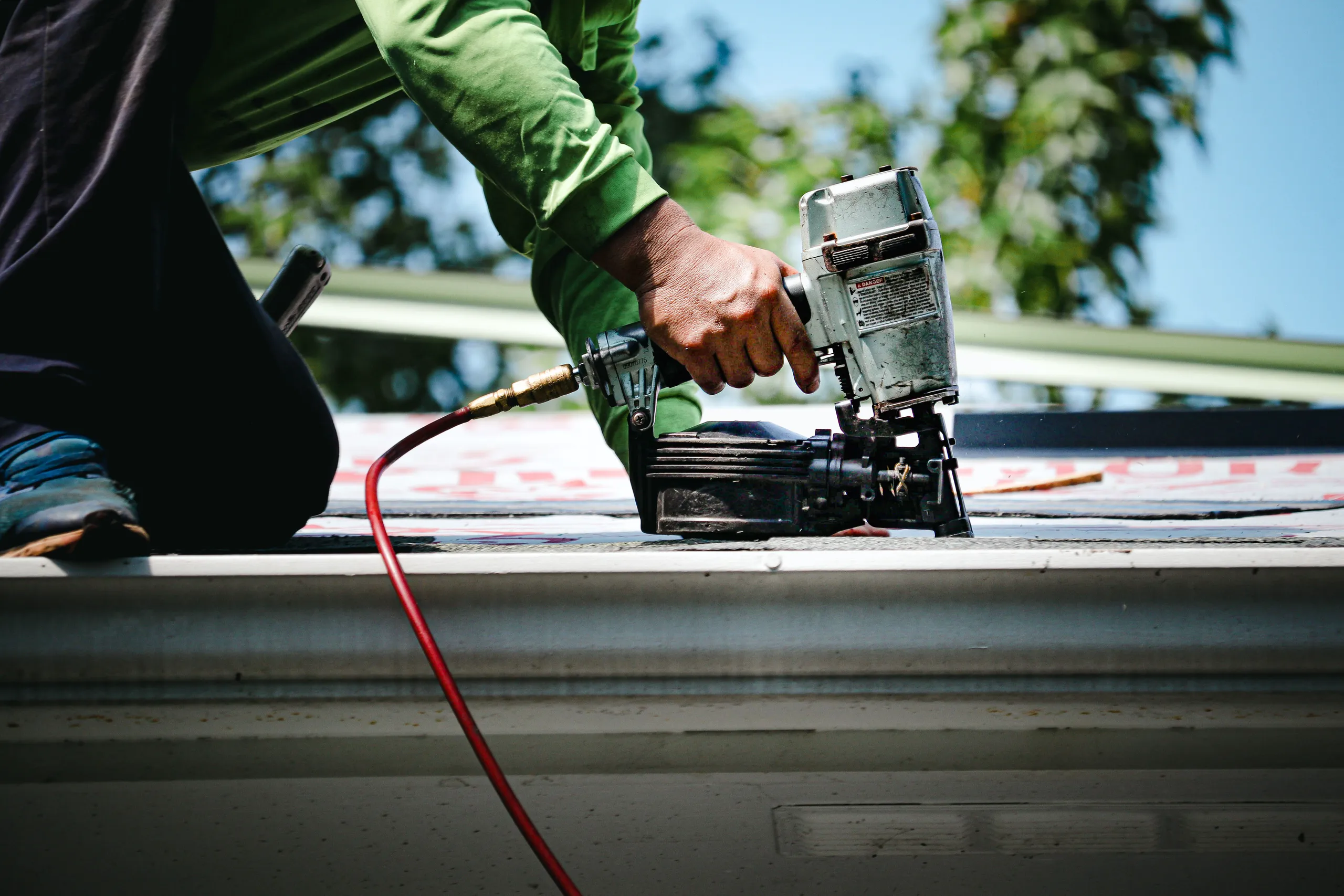 Worker using a pneumatic nail gun for roof replacement on a sunny day