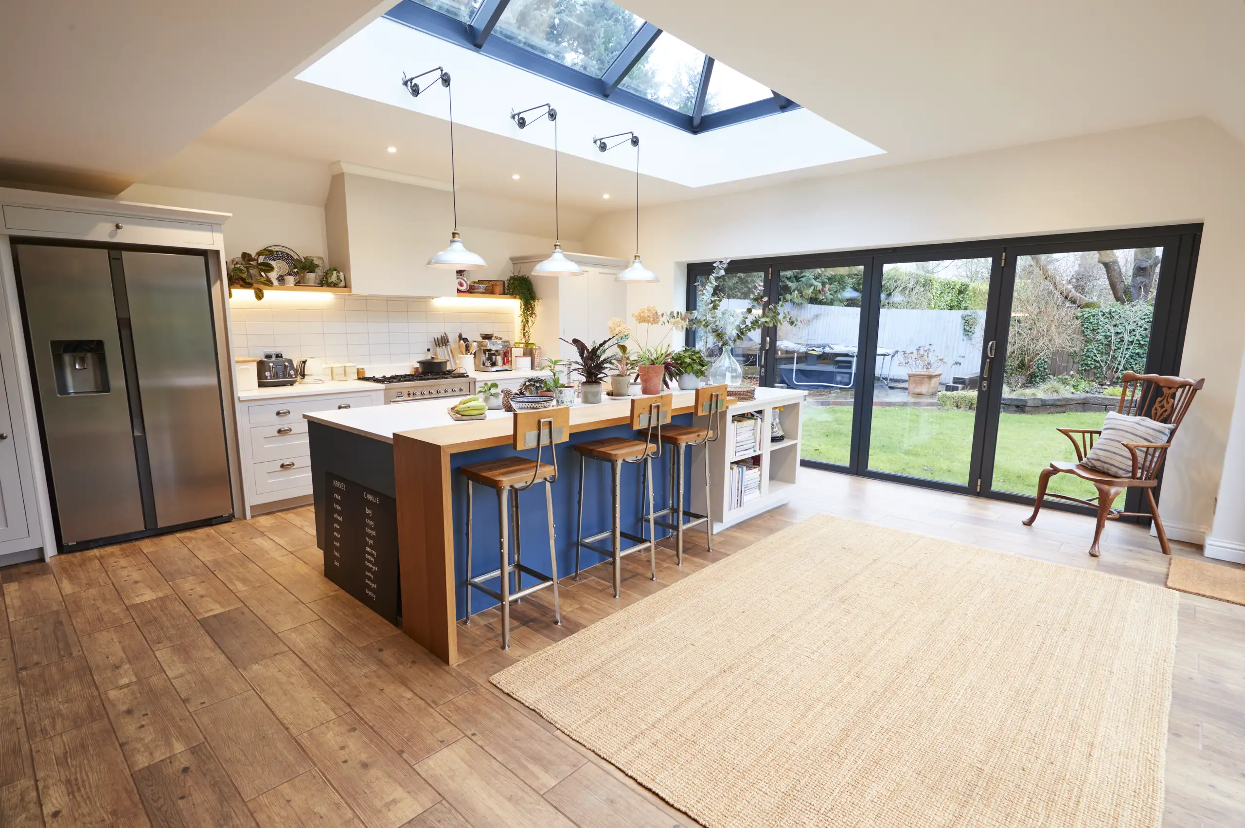 Modern kitchen with wooden flooring, island, and large windows showing outdoor garden