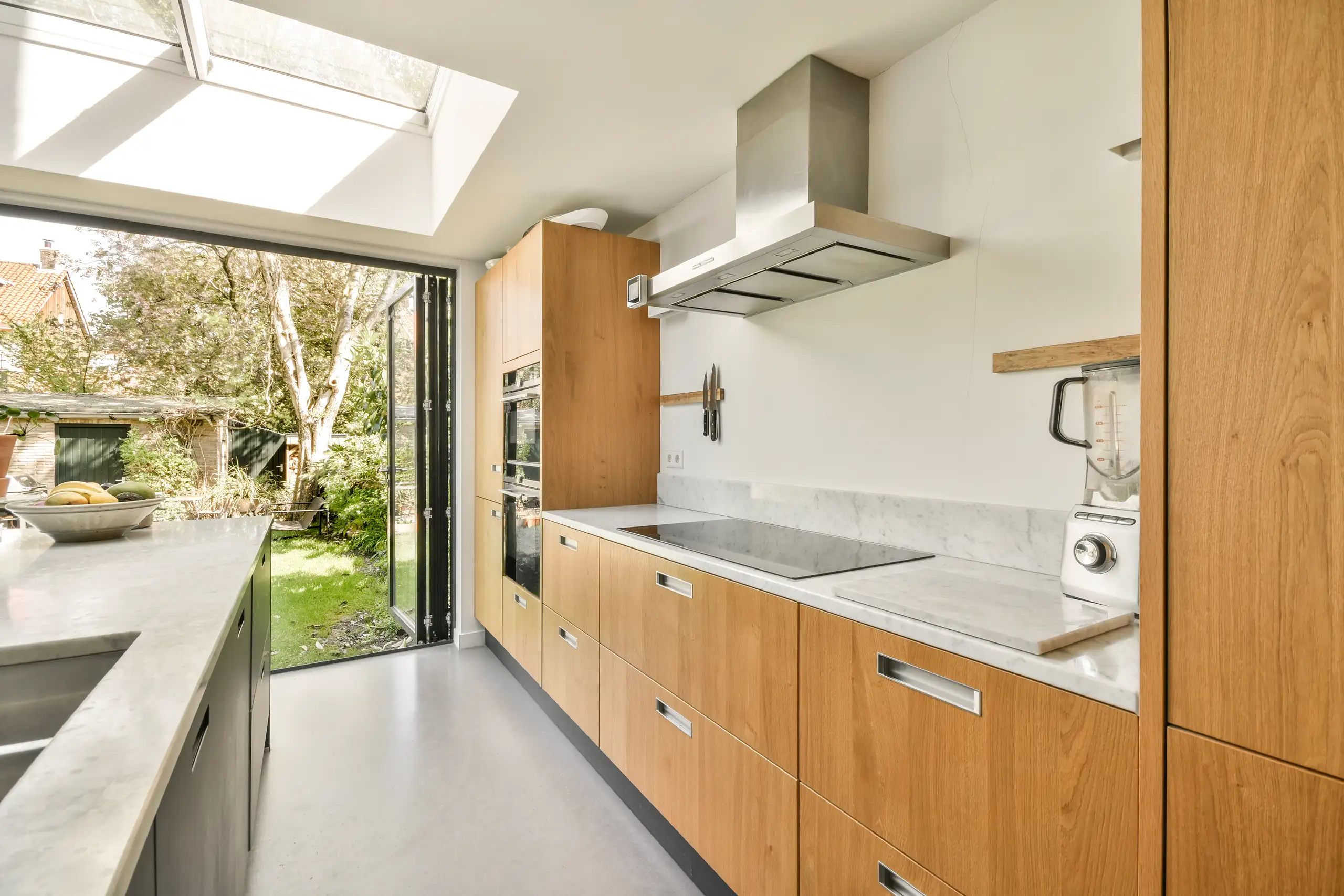 Modern kitchen with wooden cabinets, a countertop, and a garden view through large glass doors