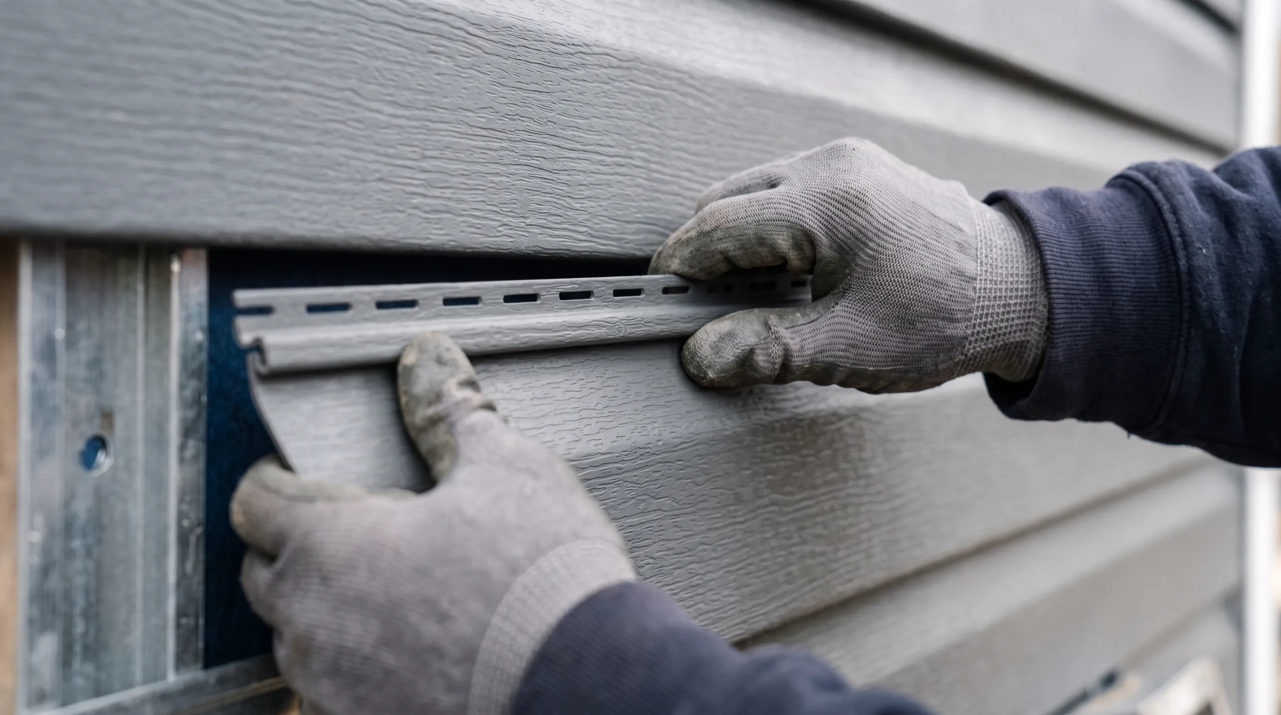 A worker installing siding on a wall, focusing on precise alignment with gloves on