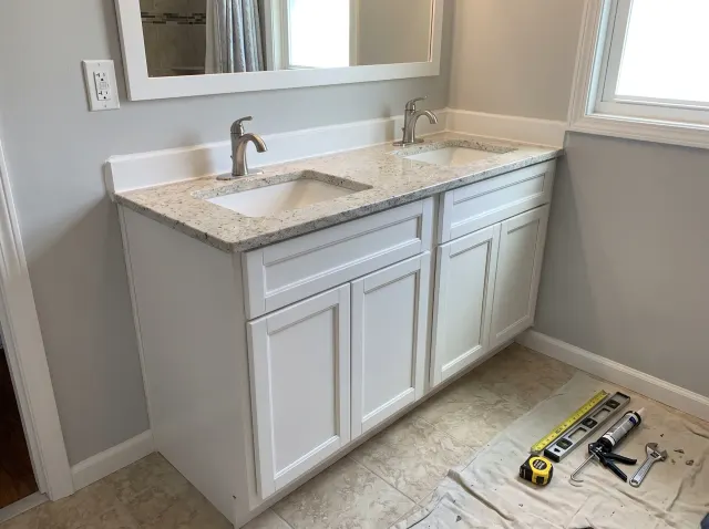 Newly installed double vanity with white cabinets and countertop, showcasing precise craftsmanship in bathroom renovation