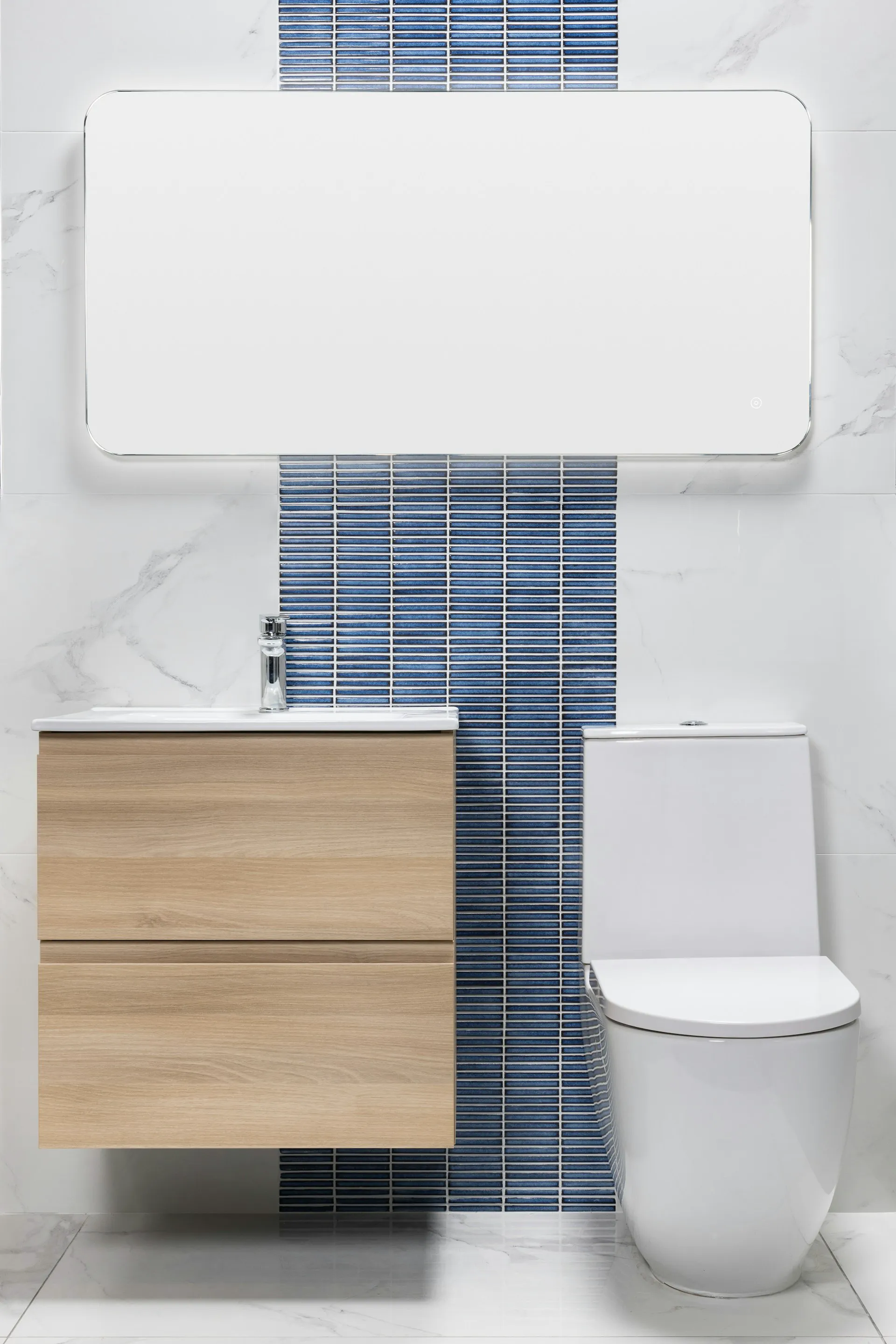 Modern bathroom with a wooden vanity and a white toilet beside blue tiled wall