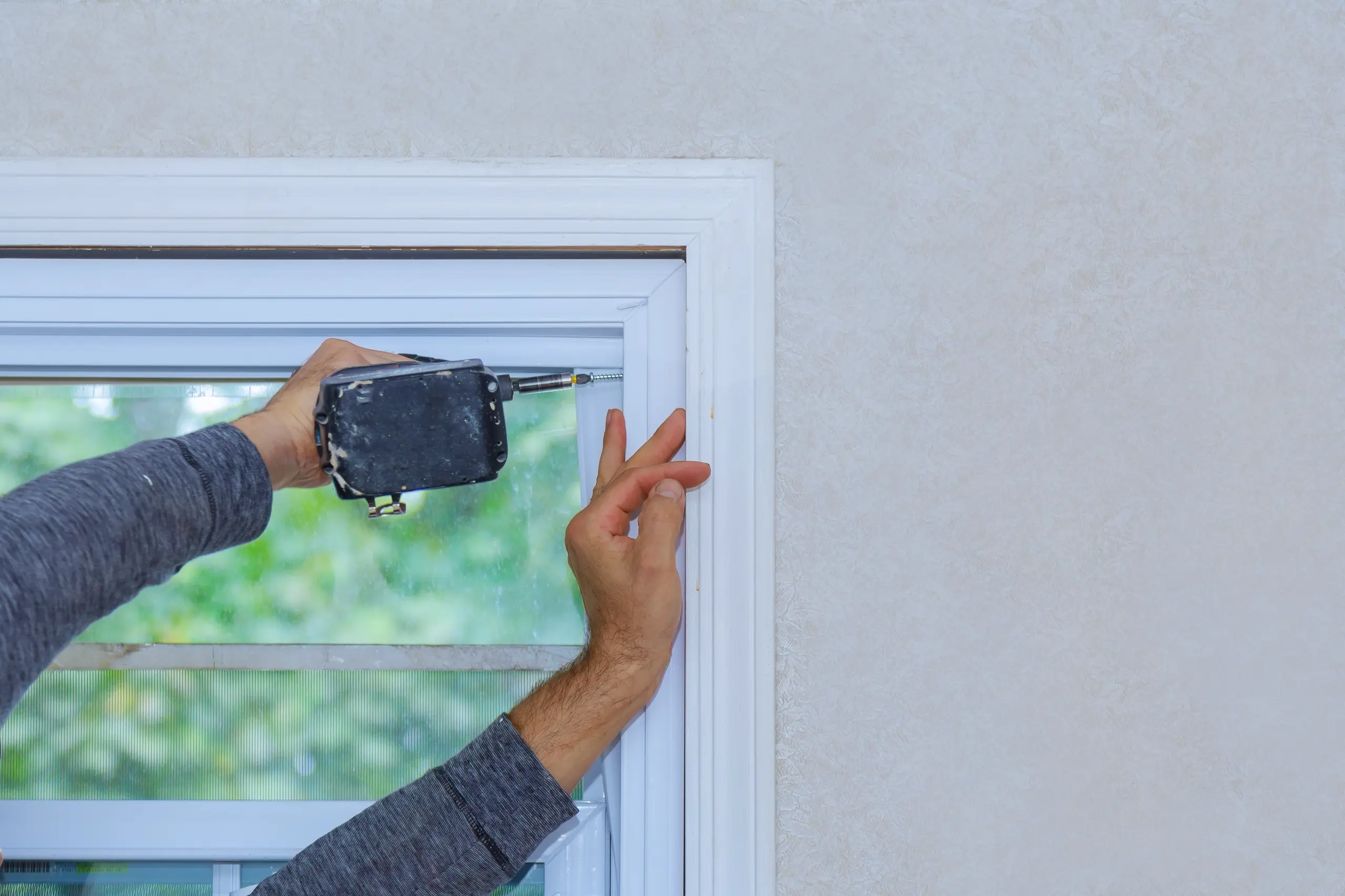 A hand installing a window trim with a cordless drill in a renovated interior space